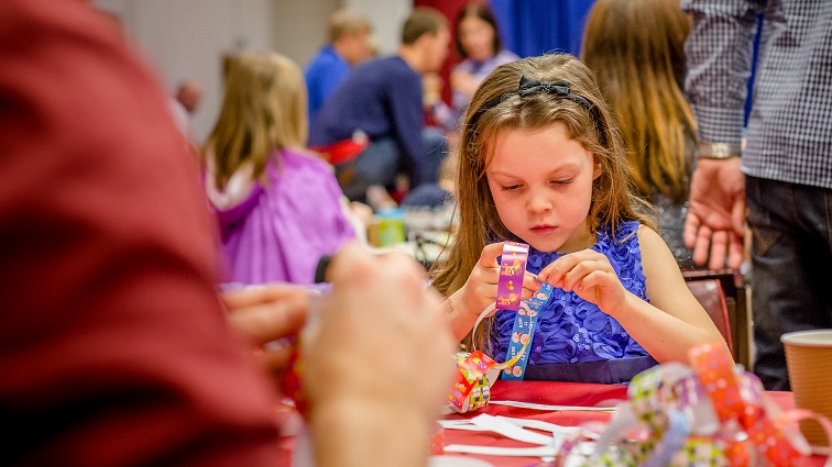 A girl is holding coloured paper and making a paper chain on a red tablecloth